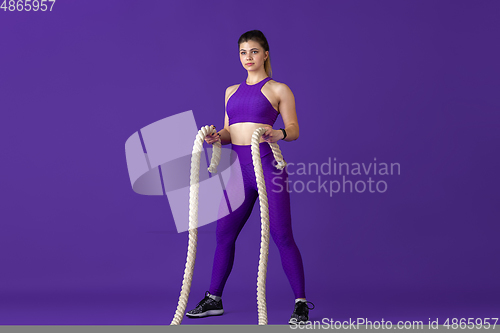 Image of Beautiful young female athlete practicing on purple studio background, monochrome portrait