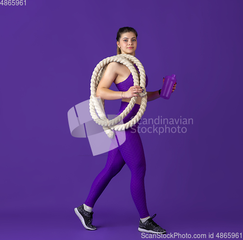 Image of Beautiful young female athlete practicing on purple studio background, monochrome portrait