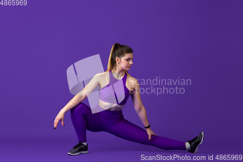 Image of Beautiful young female athlete practicing on purple studio background, monochrome portrait