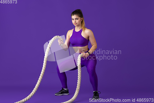 Image of Beautiful young female athlete practicing on purple studio background, monochrome portrait