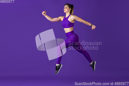 Image of Beautiful young female athlete practicing on purple studio background, monochrome portrait