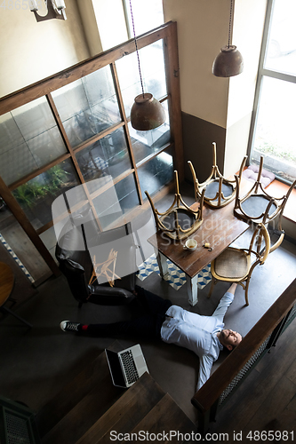 Image of Public institutions closed due to COVID-19 or Coronavirus outbreak lockdown, stressed owner of small business alone lying down the floor in his cafe, restaurant, bar