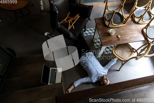 Image of Public institutions closed due to COVID-19 or Coronavirus outbreak lockdown, stressed owner of small business alone lying down the floor in his cafe, restaurant, bar