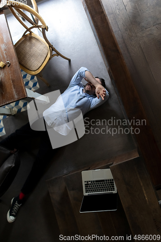 Image of Public institutions closed due to COVID-19 or Coronavirus outbreak lockdown, stressed owner of small business alone lying down the floor in his cafe, restaurant, bar