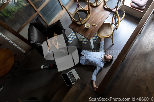 Image of Public institutions closed due to COVID-19 or Coronavirus outbreak lockdown, stressed owner of small business alone lying down the floor in his cafe, restaurant, bar