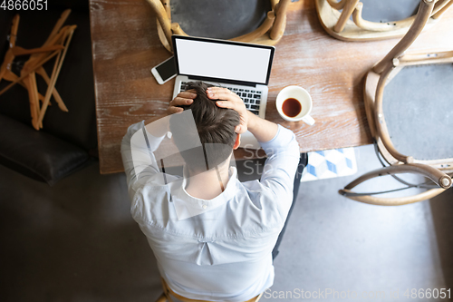 Image of Public institutions closed due to COVID-19 or Coronavirus outbreak lockdown, stressed owner of small business alone in his cafe, looking for solution, top view