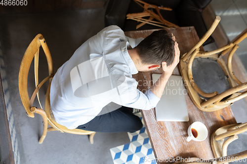 Image of Public institutions closed due to COVID-19 or Coronavirus outbreak lockdown, stressed owner of small business alone in his cafe, looking for solution, top view