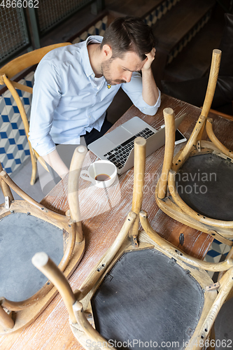 Image of Public institutions closed due to COVID-19 or Coronavirus outbreak lockdown, stressed owner of small business alone in his cafe, restaurant, bar, shocked and despair