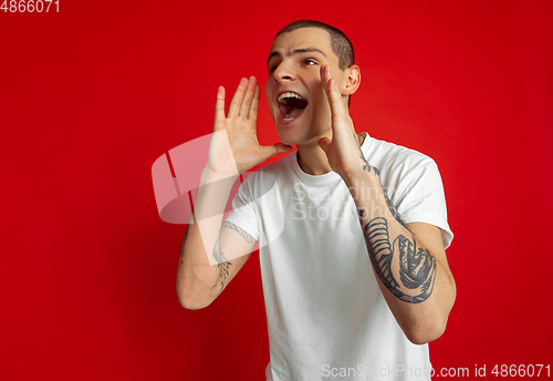 Image of Caucasian young man\'s portrait on red studio background, emotinal and expressive