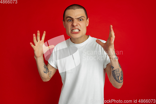 Image of Caucasian young man\'s portrait on red studio background, emotinal and expressive