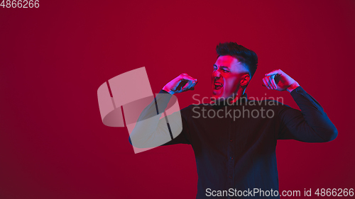 Image of Caucasian man\'s portrait isolated on red studio background in purple-blue neon light, emotional and beautiful