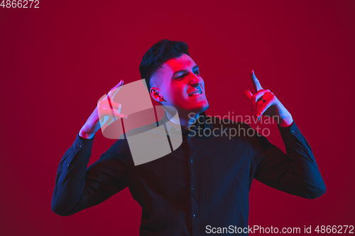 Image of Caucasian man\'s portrait isolated on red studio background in purple-blue neon light, emotional and beautiful