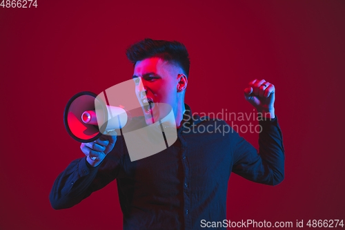 Image of Caucasian man\'s portrait isolated on red studio background in purple-blue neon light, emotional and beautiful
