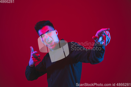 Image of Caucasian man\'s portrait isolated on red studio background in purple-blue neon light, emotional and beautiful