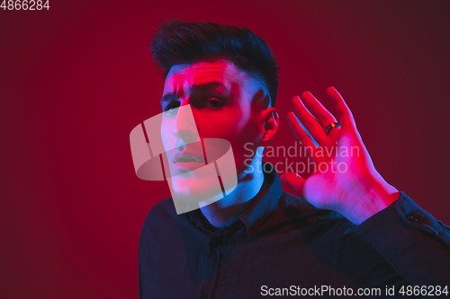 Image of Caucasian man\'s portrait isolated on red studio background in purple-blue neon light, emotional and beautiful