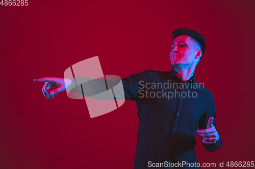 Image of Caucasian man\'s portrait isolated on red studio background in purple-blue neon light, emotional and beautiful