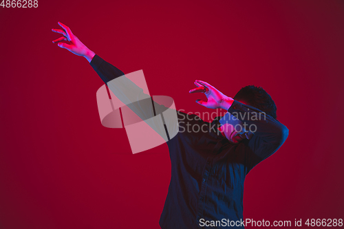 Image of Caucasian man\'s portrait isolated on red studio background in purple-blue neon light, emotional and beautiful