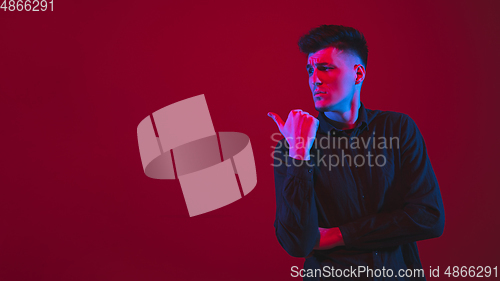 Image of Caucasian man\'s portrait isolated on red studio background in purple-blue neon light, emotional and beautiful
