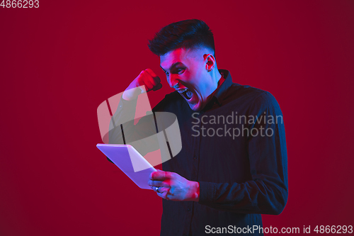 Image of Caucasian man\'s portrait isolated on red studio background in purple-blue neon light, emotional and beautiful