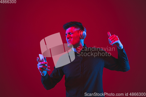 Image of Caucasian man\'s portrait isolated on red studio background in purple-blue neon light, emotional and beautiful