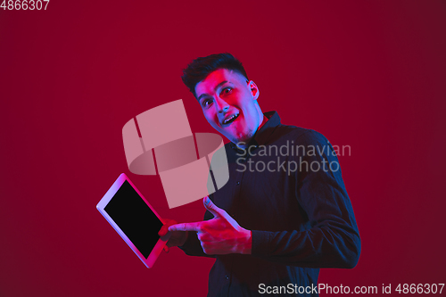 Image of Caucasian man\'s portrait isolated on red studio background in purple-blue neon light, emotional and beautiful
