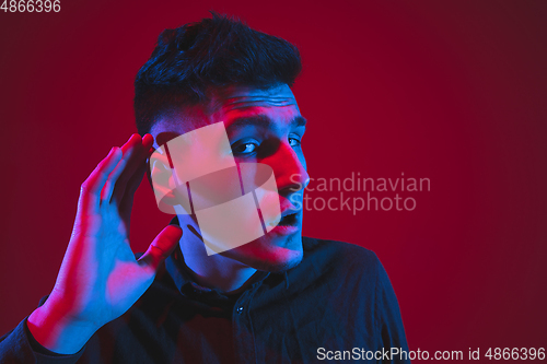 Image of Caucasian man\'s portrait isolated on red studio background in purple-blue neon light, emotional and beautiful