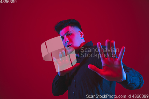 Image of Caucasian man\'s portrait isolated on red studio background in purple-blue neon light, emotional and beautiful