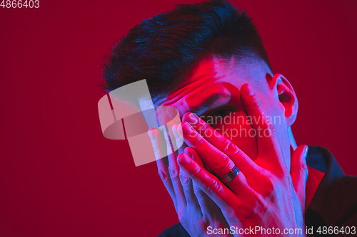 Image of Caucasian man\'s portrait isolated on red studio background in purple-blue neon light, emotional and beautiful, close up