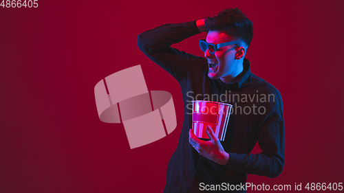 Image of Caucasian man\'s portrait isolated on red studio background in purple-blue neon light, emotional and beautiful, looking throught 3D-eyewear, cinema