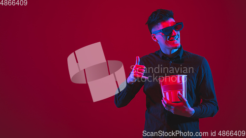 Image of Caucasian man\'s portrait isolated on red studio background in purple-blue neon light, emotional and beautiful, looking throught 3D-eyewear, cinema