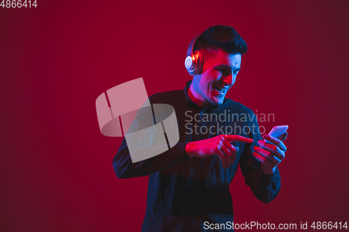 Image of Caucasian man\'s portrait isolated on red studio background in purple-blue neon light, emotional and beautiful