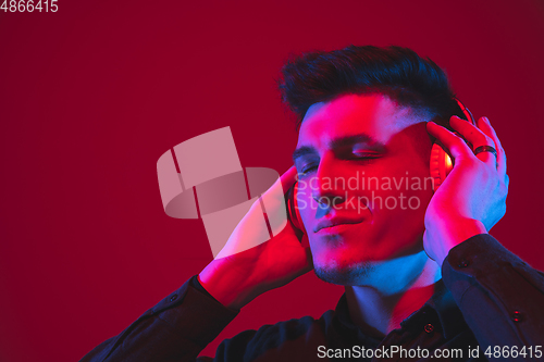 Image of Caucasian man\'s portrait isolated on red studio background in purple-blue neon light, emotional and beautiful, close up