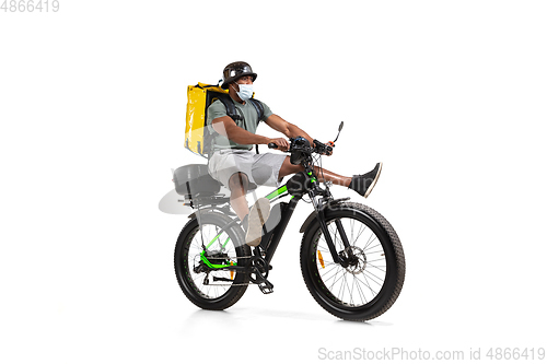 Image of Too much orders. Contacless delivery service during quarantine. Man delivers food and shopping bags during isolation, wearing helmet and face mask.