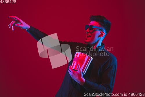 Image of Caucasian man\'s portrait isolated on red studio background in purple-blue neon light, emotional and beautiful, looking throught 3D-eyewear, cinema