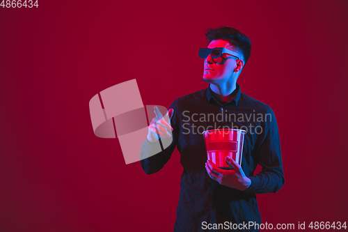 Image of Caucasian man\'s portrait isolated on red studio background in purple-blue neon light, emotional and beautiful, looking throught 3D-eyewear, cinema