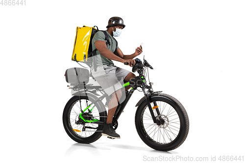 Image of Too much orders. Contacless delivery service during quarantine. Man delivers food and shopping bags during isolation, wearing helmet and face mask.