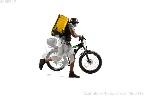 Image of Too much orders. Contacless delivery service during quarantine. Man delivers food and shopping bags during isolation, wearing helmet and face mask.