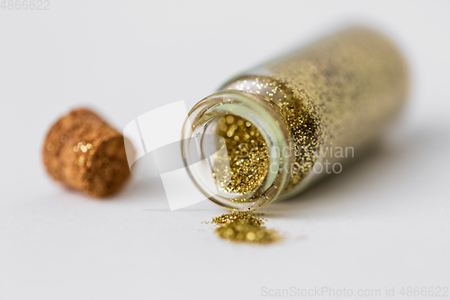 Image of golden glitters poured from small glass bottle