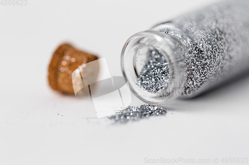 Image of silver glitters poured from small glass bottle