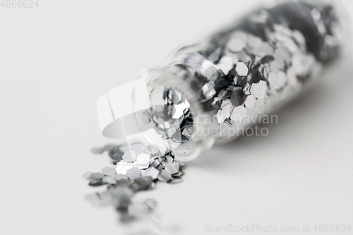 Image of silver glitters poured from small glass bottle