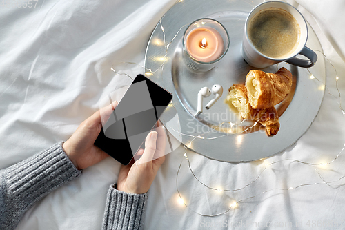 Image of hands with smartphone, croissant and coffee in bed