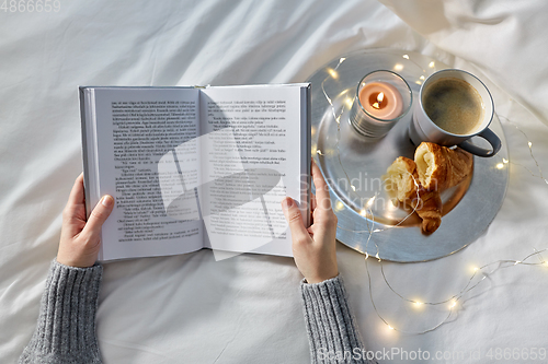 Image of hands of woman with book, coffee and croissants