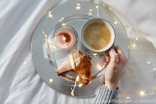 Image of hand of woman drinking coffee with croissant