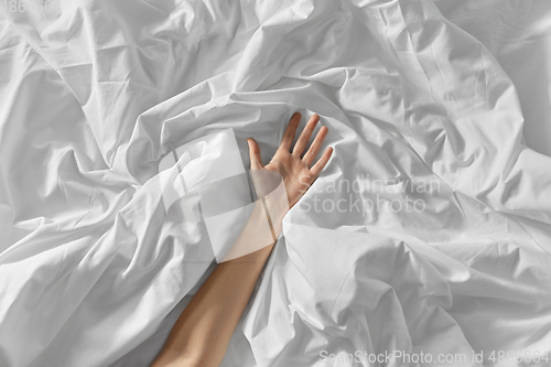 Image of hand of woman lying on rumpled bed sheet