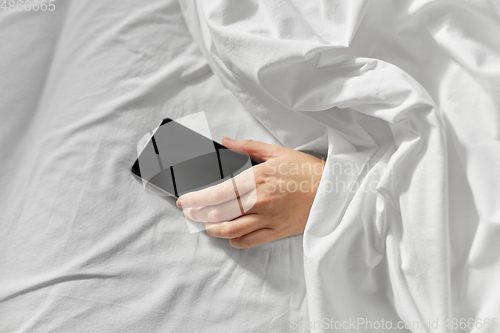 Image of hand of woman lying in bed with smartphone