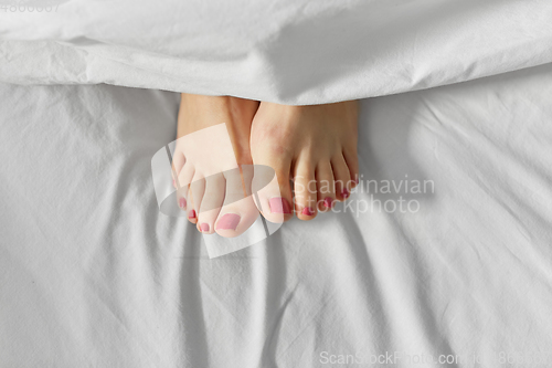 Image of feet of woman lying in bed under white blanket