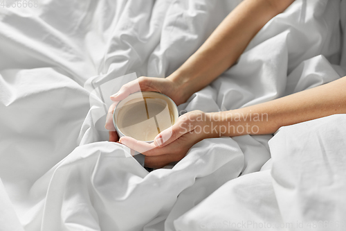 Image of hands of woman with cup of coffee in bed