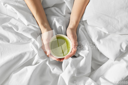 Image of hands of woman with cup of matcha tea in bed