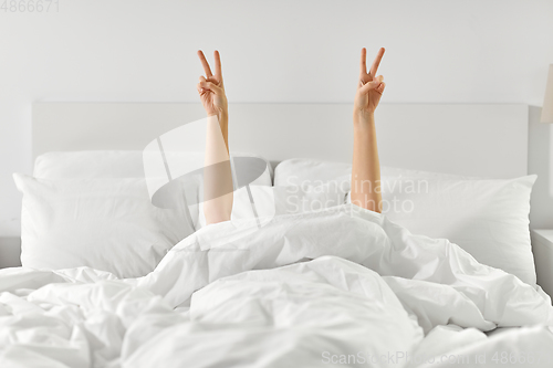 Image of hands of woman lying in bed and showing peace