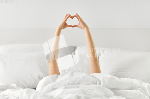 Image of hands of woman lying in bed and making heart shape